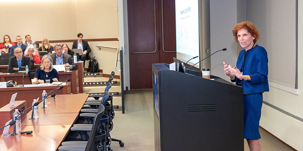 Keynote speaker Loretta Mester, then president and CEO of the Federal Reserve Bank of Cleveland, stands behind a podium in a bright royal blue suit speaking about payments modernization to rows of seated attendees in an auditorium during the 2022 Chicago Payments Symposium.