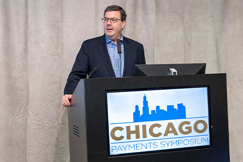 Mark Gould, chief payments executive, Federal Reserve Financial Services, stands behind a podium to introduce a keynote speaker during the 2023 Chicago Payments Symposium.