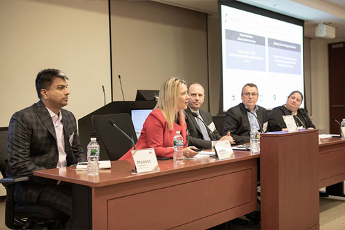 Five payment security panelists sit at a desk in front of microphones, discussing scams and fraud during the 2024 Chicago Payments Symposium.